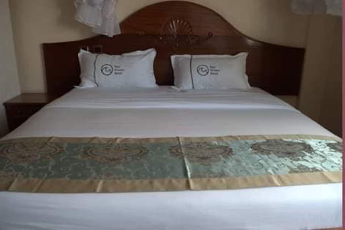 A neatly made bed with a patterned bedspread and two pillows with a circular logo.