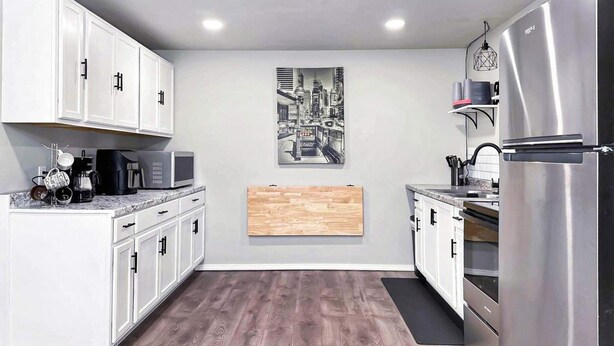 Eine moderne Küche mit weißen Schränken, einem Edelstahl-Kühlschrank und einem Stadtbild an der Wand.