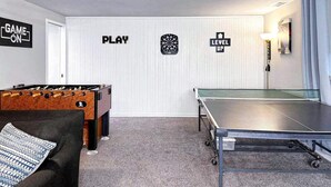 Ein Zimmer mit Tischfußball, Pongtisch und Wanddekorationen, darunter die Aufschriften 'GAME ON' und 'LEVEL UP'.