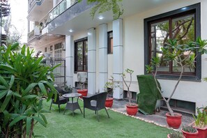 A courtyard with artificial grass, outdoor furniture, potted plants, and a building with balconies and windows. - Yuhi Suites (Gurugram)