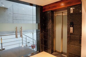 An elevator with a control panel, a glass door, and a wooden panel above it. - Yuhi Suites (Gurugram)