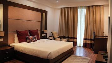 A large bed with a headboard, a bedside table, a chair, a desk, and a TV.
