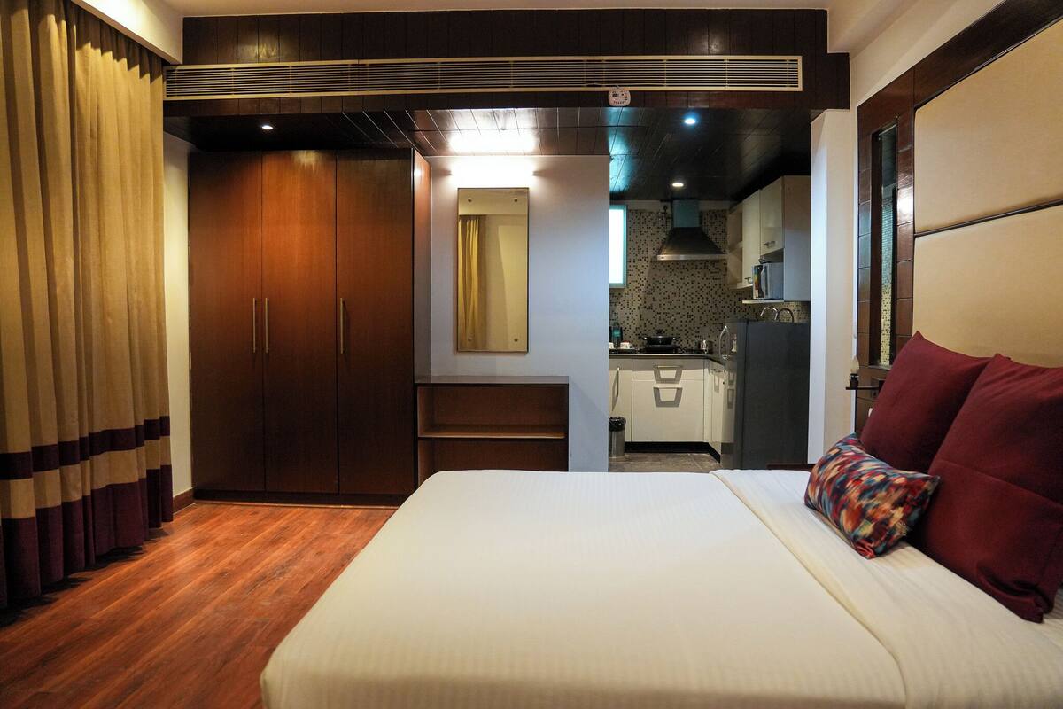 Una habitación de hotel con cama, armario, espejo, kitchenette pequeña y baño.