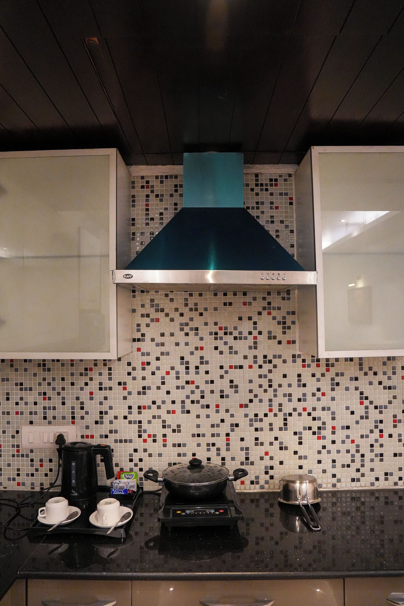 A kitchen with a tiled backsplash, a stove, a coffee maker, and a kettle.