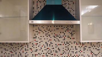 A kitchen with a tiled backsplash, a stove, a coffee maker, and a kettle.