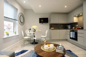 A modern kitchen with white cabinets, a built-in oven, and a flat-screen TV.