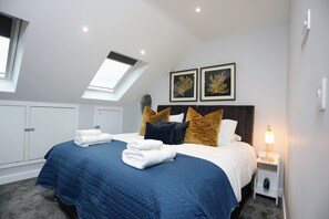 A bedroom with a bed, a nightstand, a lamp, and a skylight.