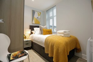 Une chambre moderne avec un lit, une table de chevet, une lampe et une fenêtre avec des stores.
