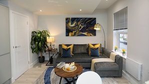 Un salon moderne avec un canapé gris, des coussins bleus, une table basse ronde et un grand tableau abstrait accroché au mur.