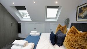 Une chambre moderne avec des fenêtres de toit, un lit agrémenté de coussins bleus et dorés, et des serviettes soigneusement pliées.