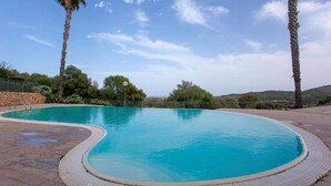 Une piscine à l’eau d’un bleu limpide, entourée d’une terrasse en pierre et d’une rambarde en métal.