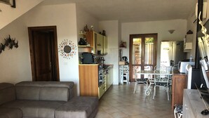 Un salon avec un canapé gris, une cuisine avec des meubles en bois et un coin repas avec une table et des chaises.