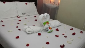 A neatly made bed with rose petals scattered across the surface, a rolled towel, and a bottle of Nivea cream. - City Wall Hotel (Nairobi)