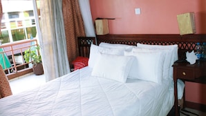 A hotel room with a large bed, a wooden headboard, a nightstand, and a view of the outside balcony. - City Wall Hotel (Nairobi)