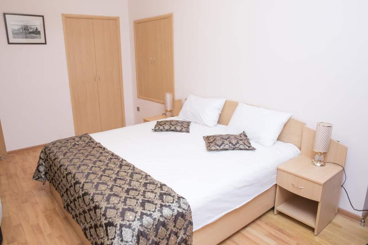 A bedroom with a bed, two wooden wardrobes, a bedside table with a lamp, and a patterned bedspread.