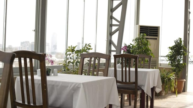 A restaurant with tables covered in white tablecloths, wooden chairs, and potted plants. - City Wall Hotel (Nairobi)