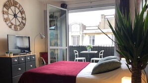 A bedroom with a bed, a TV on a dresser, a balcony with chairs, and a large wall clock. - Studio with balcony & free parking (Tours)