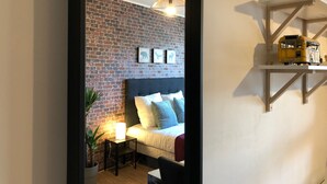 A bedroom with a brick wall, a bed with pillows, a bedside table with a lamp, and a shelf with a model bus. - Studio with balcony & free parking (Tours)