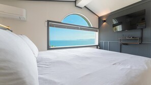Et soveværelse med en stor seng, et vindue med havudsigt, et ophængt tv og en loftslampe.