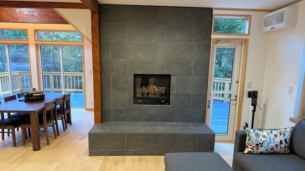 A living room with a stone fireplace, wooden dining table, and grey sofa. - Picollo Mondo (Yamanakako)