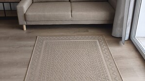A beige sofa in a room with a wooden floor and a woven rug. - Apartments Melita (Zadar)