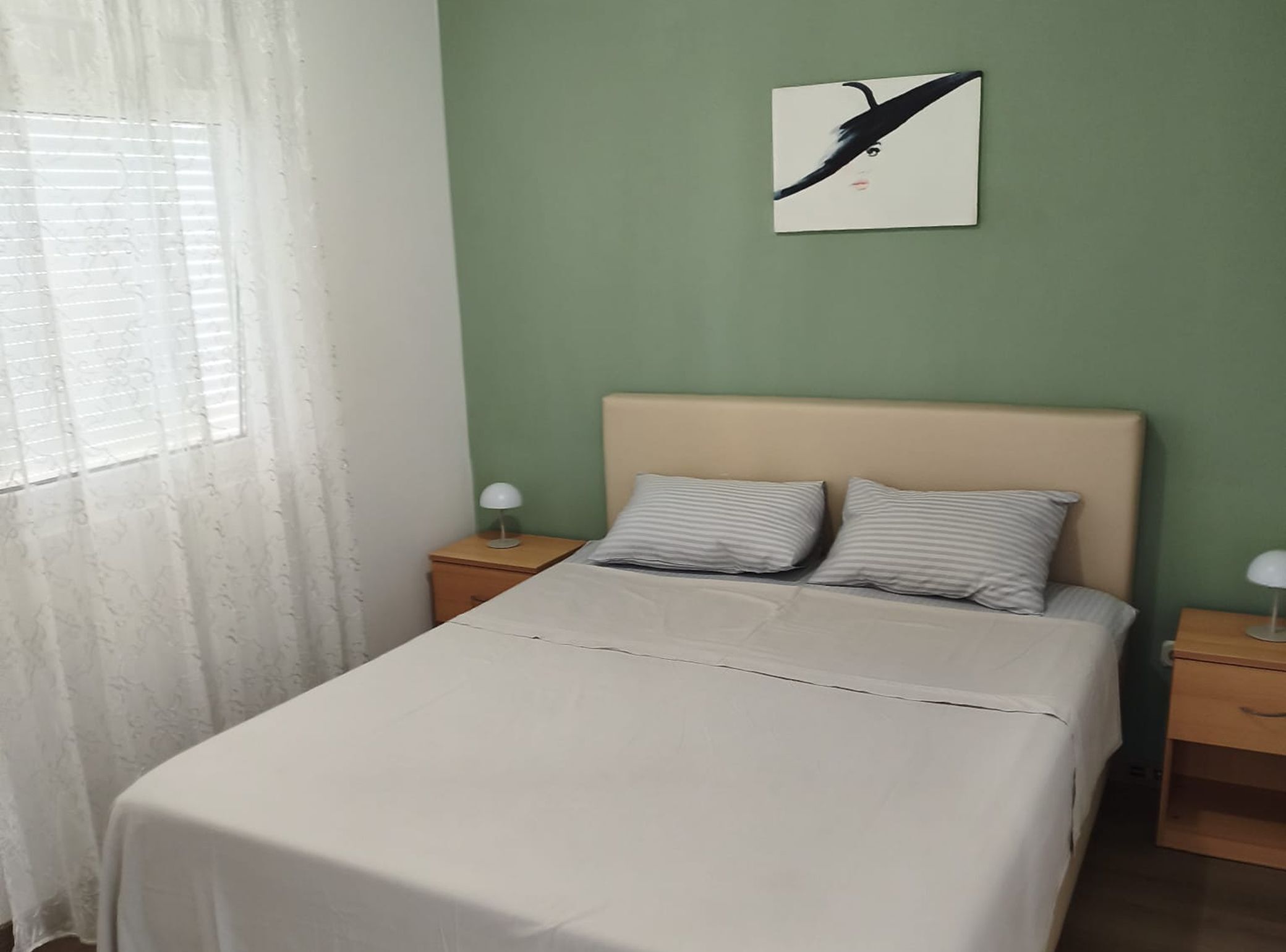 A bed with a white bedspread, two pillows, a nightstand with a lamp, and a wall-mounted picture.