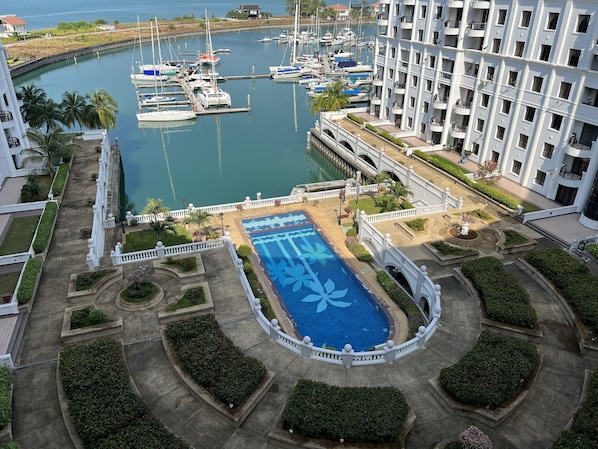 A marina with boats docked, a swimming pool with a floral design, and a white building with balconies.