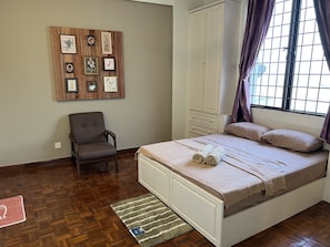 A bedroom with a bed, a chair, a wardrobe, and a wall with framed pictures.