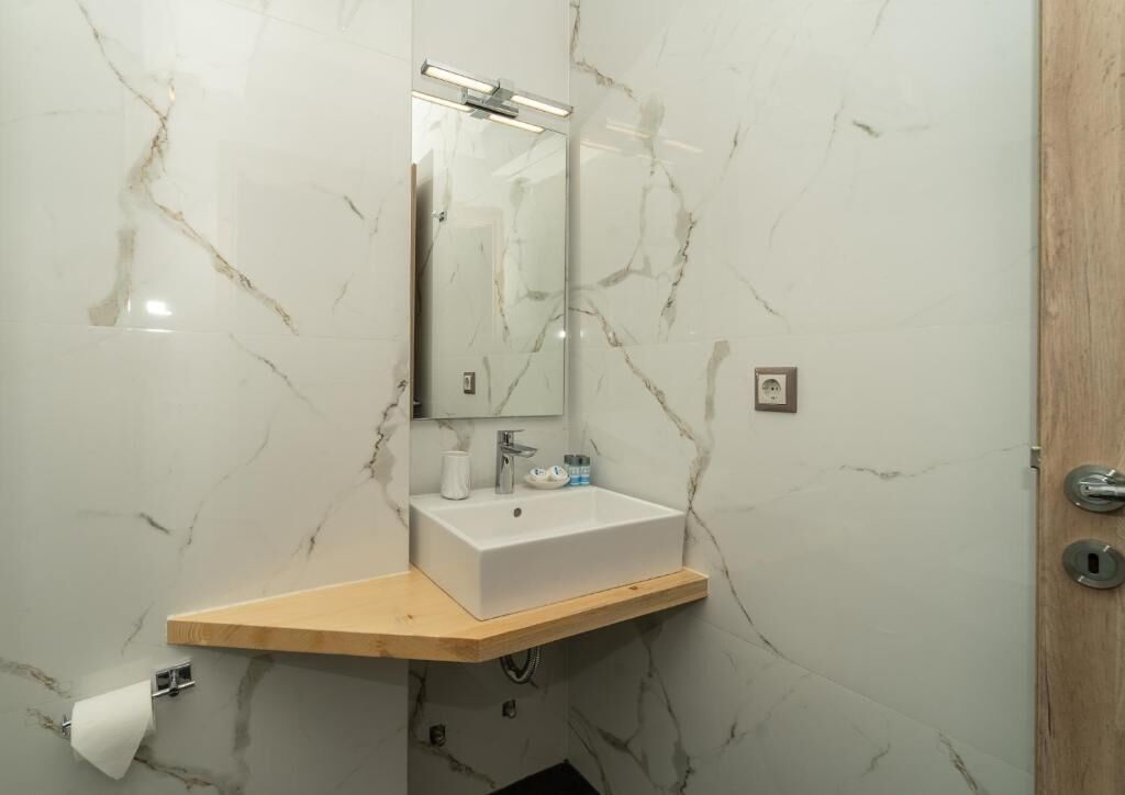 A bathroom with a marble wall, a wooden countertop, a sink, a mirror, and a toilet paper holder.