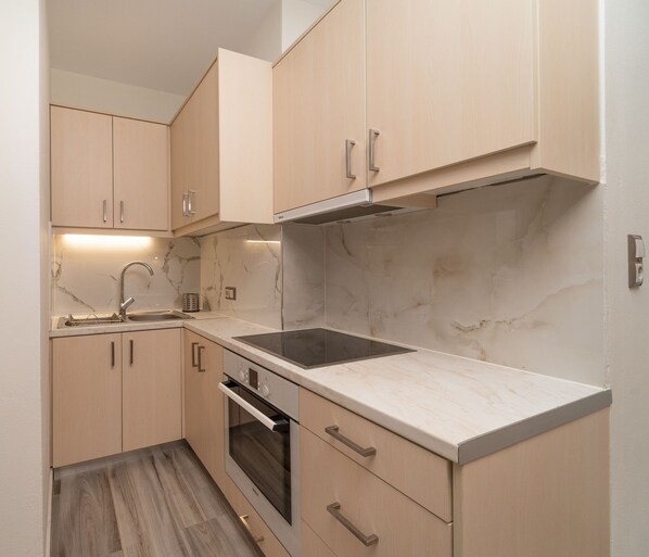 A compact kitchen with light wood cabinets, a stainless steel sink, a built-in oven, and a marble countertop. - Carlos Mansion Luxury Suites (Pylos-Nestoras)