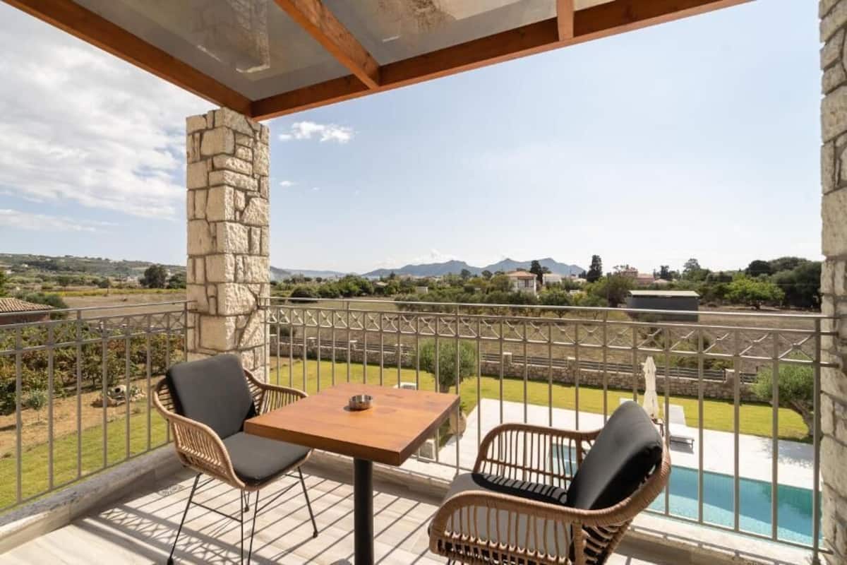 A balcony with wicker furniture and a view of a swimming pool and distant landscape.