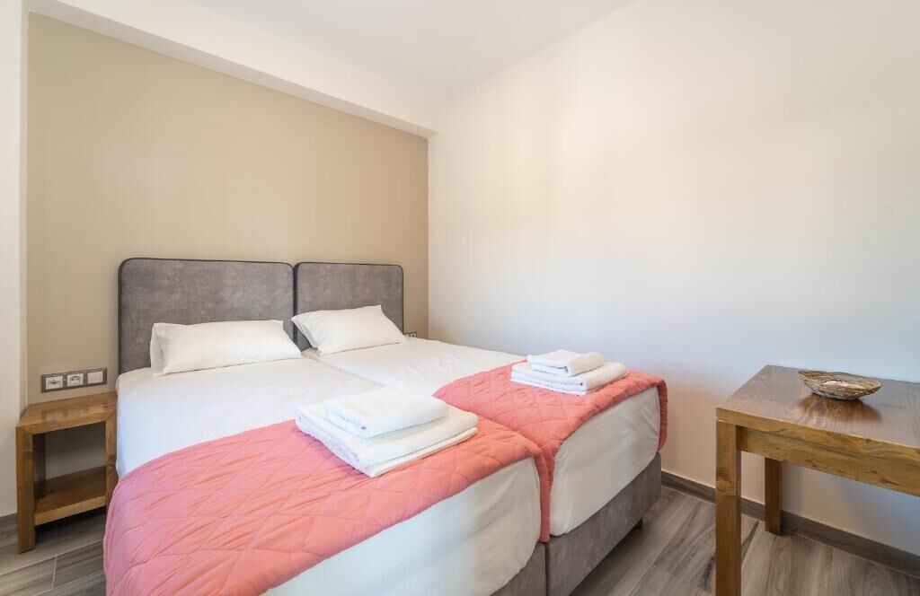 Een tweepersoonsbed met twee kussens, een houten nachtkastje, een klein tafeltje met een schaal, en een roze deken.