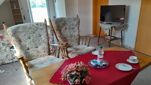 A dining area with floral-patterned sofas, a wooden dining table with a red tablecloth, a bouquet of flowers, and a television on a stand. - Vacation apartment Berta 25508 - Holiday apartment Berta, 25508 (Weener)