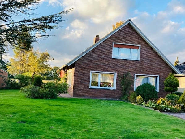 A two-story house with a brick exterior, a well-maintained lawn, and a clear sky.