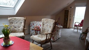 A cozy loft-style room with a high ceiling, two upholstered chairs, a small table with a red table runner, a potted plant, and a bookshelf. - Vacation apartment Berta 25508 - Holiday apartment Berta, 25508 (Weener)