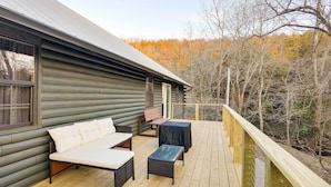 Une terrasse en bois avec des meubles d’extérieur, une table abritée et une vue sur une zone boisée.