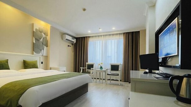 Een hotelkamer met een bed, bureau, televisie en uitzicht op de omgeving.