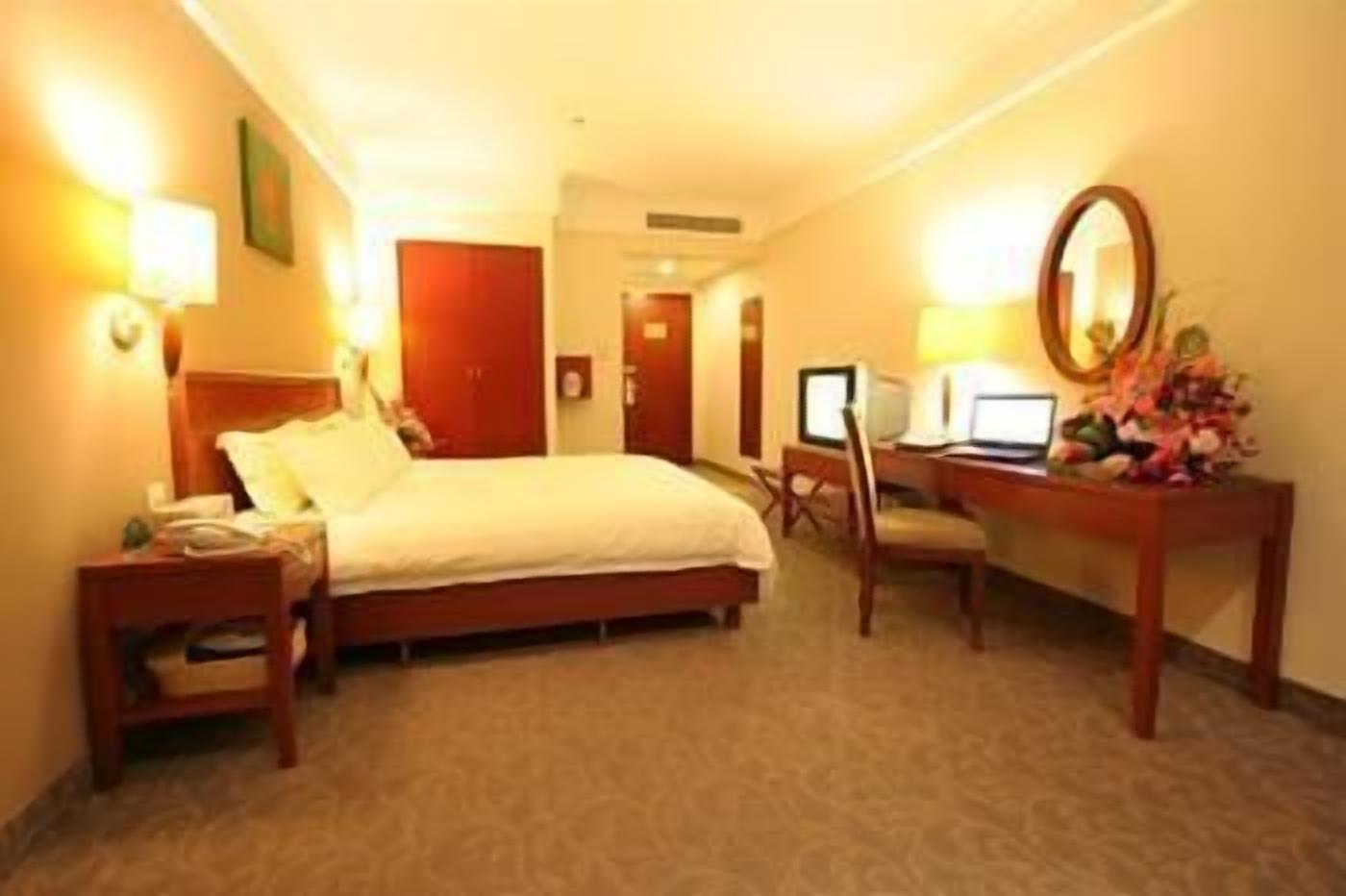 Una habitación de hotel con cama, escritorio, computadora, silla, lámpara de escritorio y espejo.