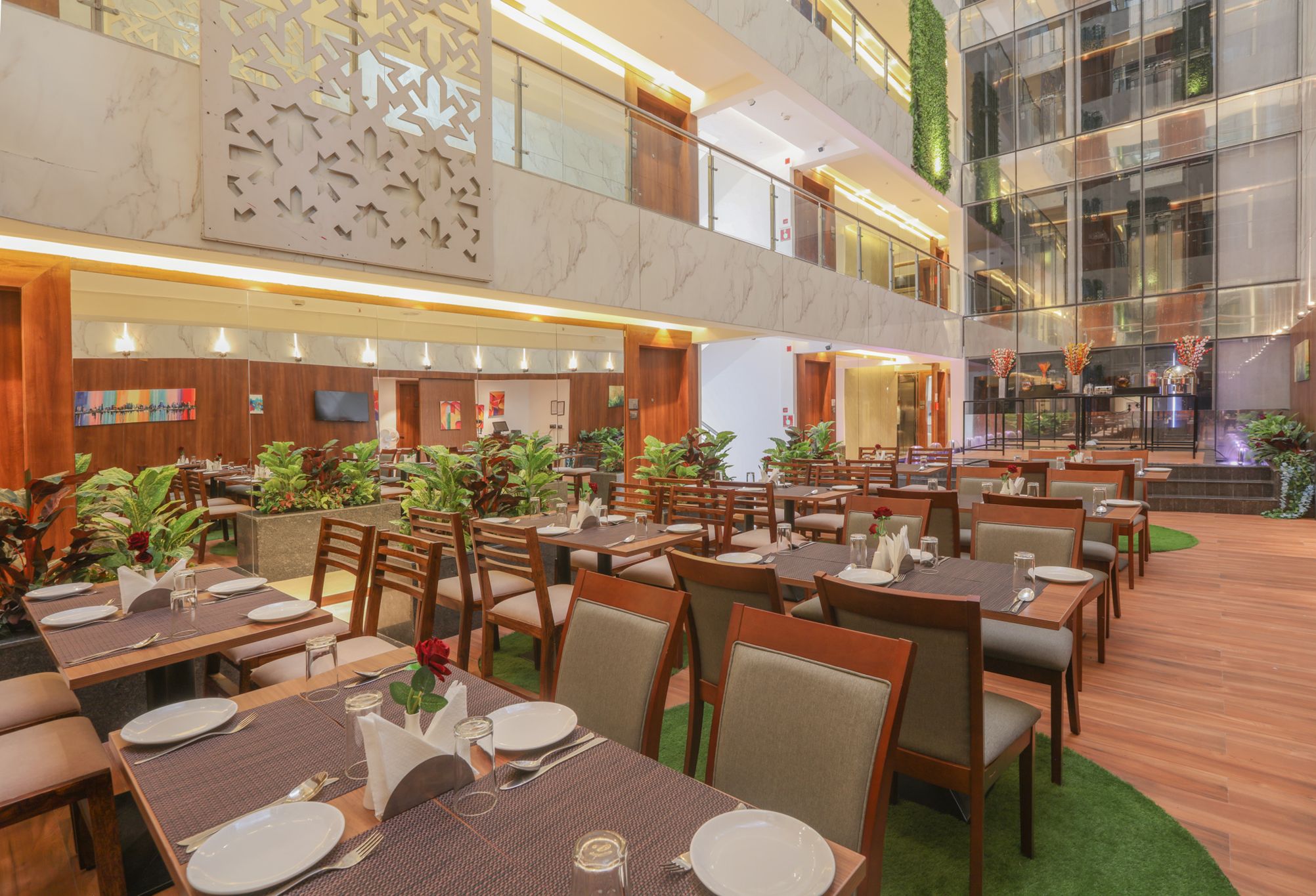 A multi-level dining area with wooden tables and chairs, a green carpeted floor, and a large glass wall with a view.