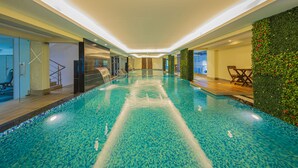 Une piscine intérieure à l’eau d’un bleu cristallin, dotée d’une terrasse en bois et d’un mur végétal.
