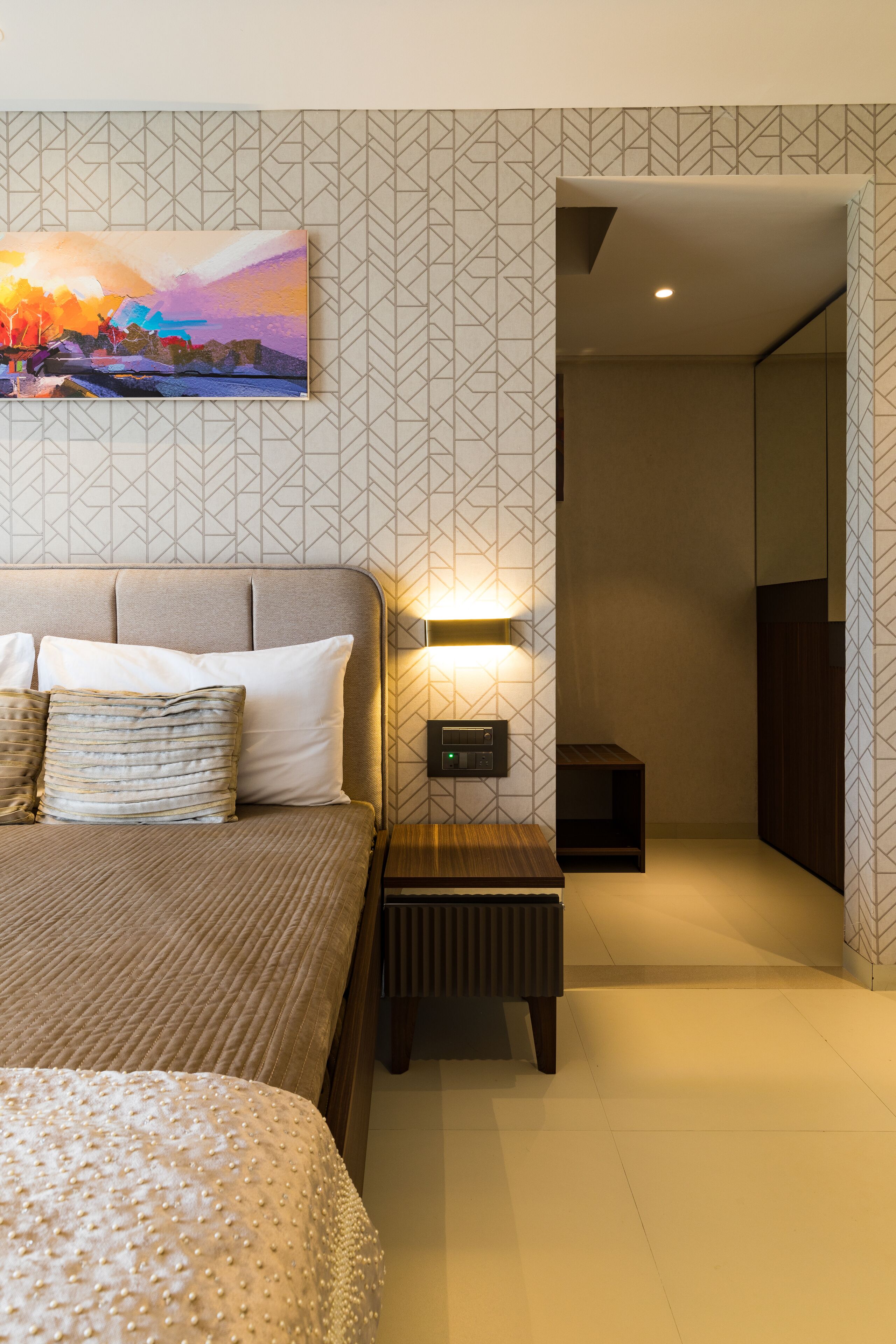 Una habitación de hotel moderna con una cama grande, una mesita de noche, un televisor montado en la pared y un cuadro sobre la cama.
