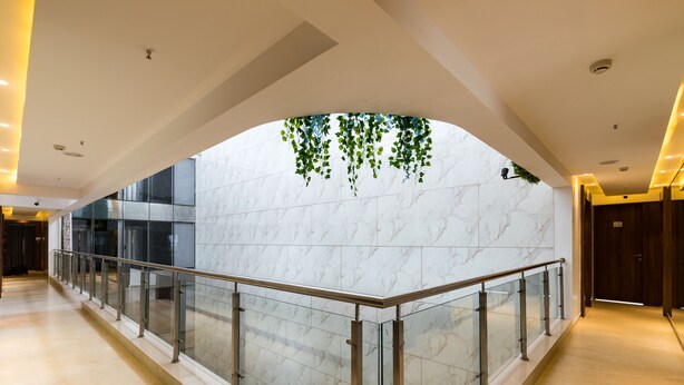 Un hall d’hôtel moderne avec un mur en marbre, une rambarde en verre et des plantes suspendues.