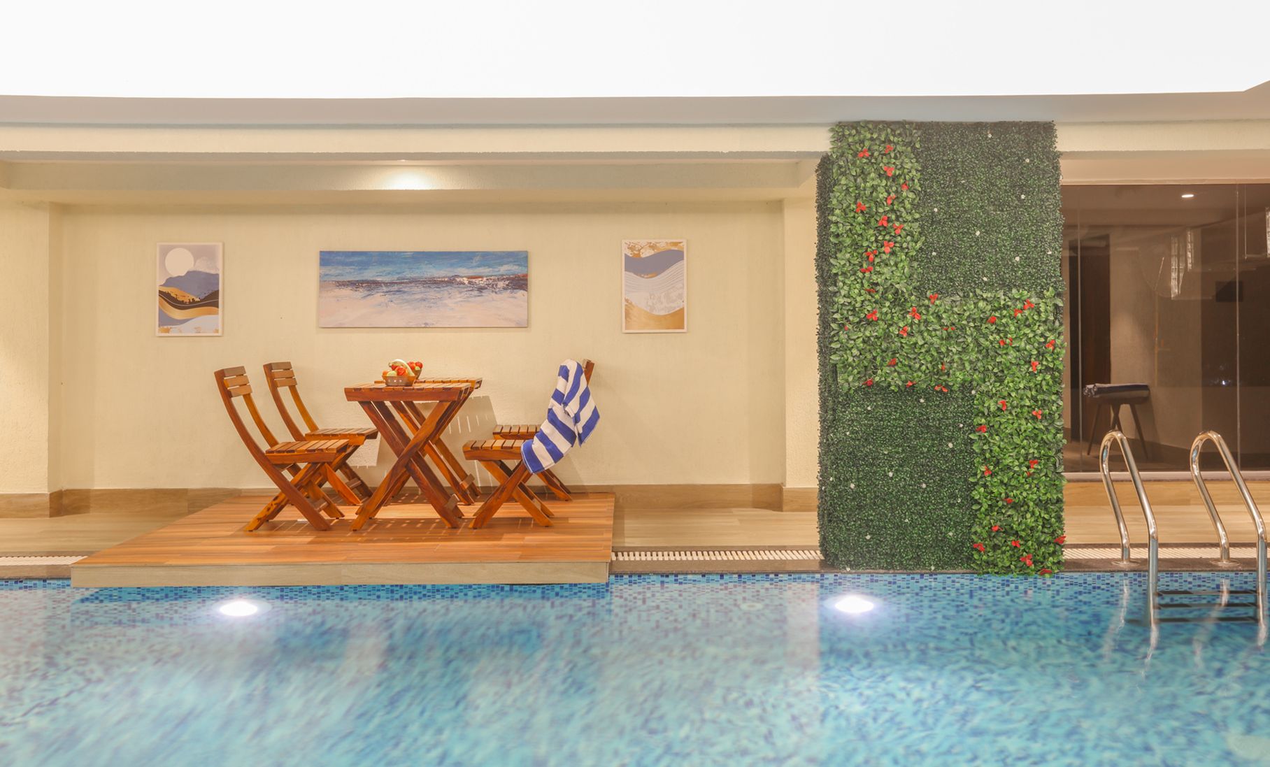 Zona junto a la piscina con una mesa y sillas, un muro decorativo con plantas y vistas a la piscina.