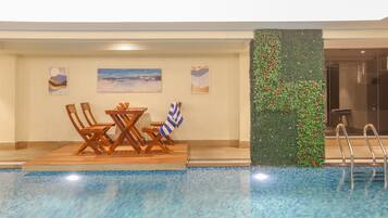 Zona junto a la piscina con una mesa y sillas, un muro decorativo con plantas y vistas a la piscina.