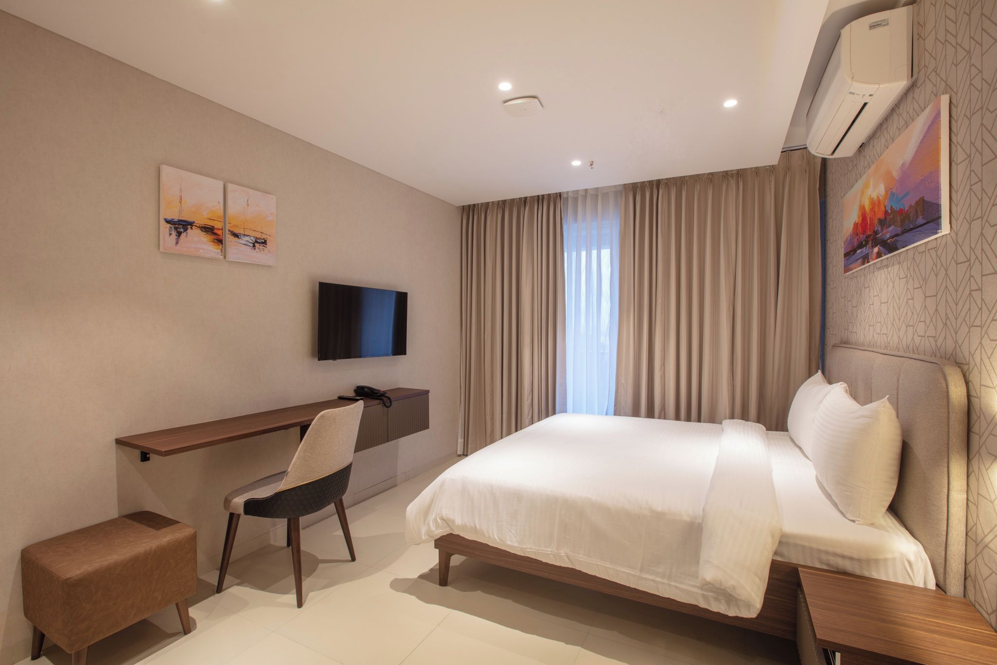 A hotel room with a bed, a desk, a chair, a TV, and a window with curtains.