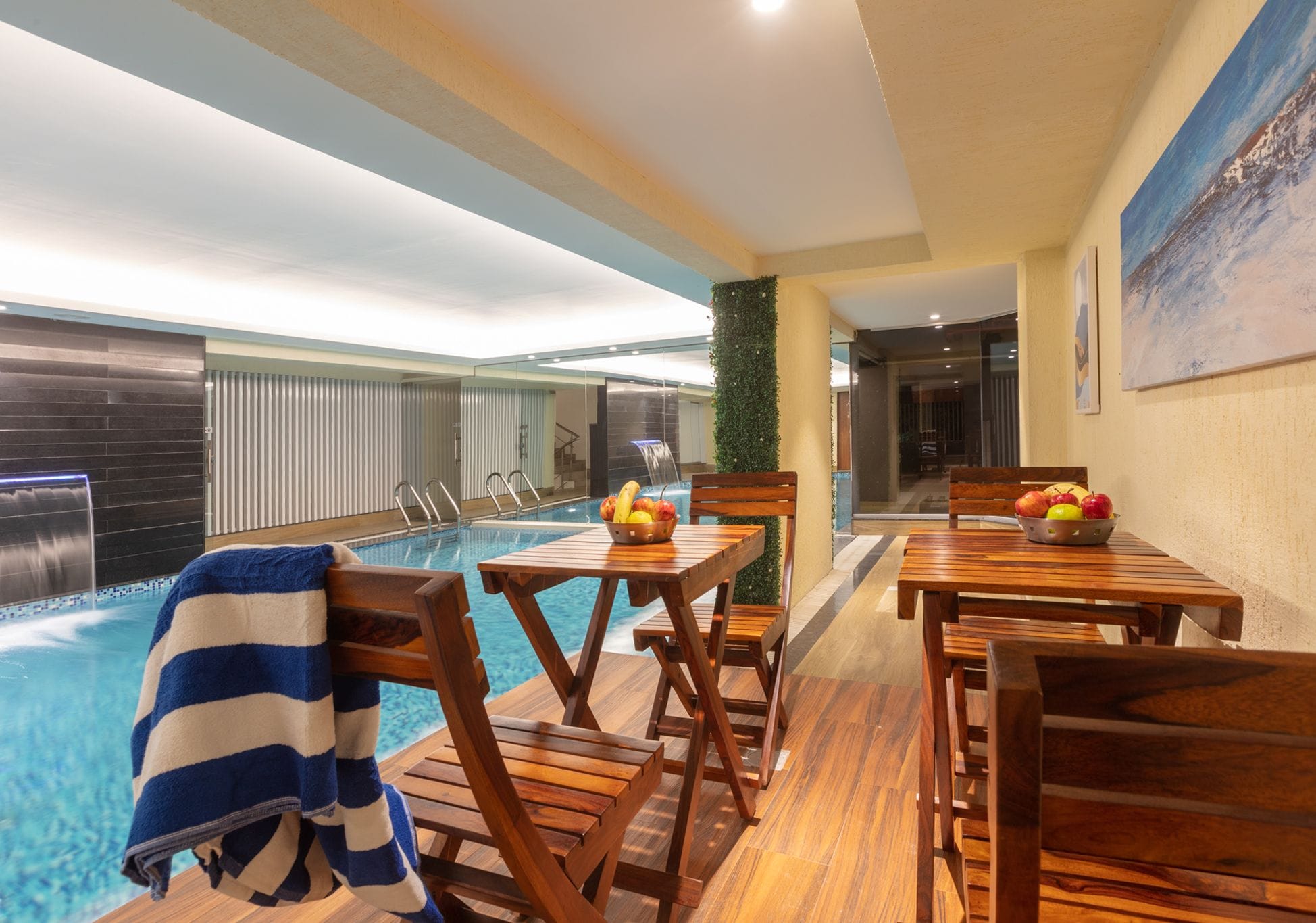 A poolside area with wooden chairs and tables, a towel, and a fruit bowl.
