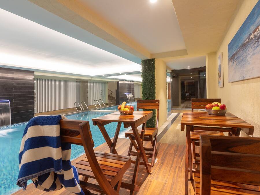 A poolside area with wooden chairs and tables, a towel, and a fruit bowl.