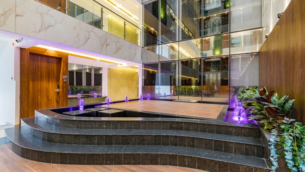 Un hall d’hôtel moderne doté d’une fontaine centrale, d’un sol en marbre et d’un atrium en verre.