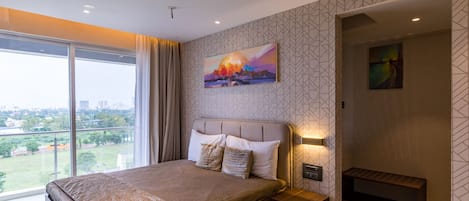 A modern bedroom with a large bed, a nightstand, a wall-mounted TV, and a city view through large windows.