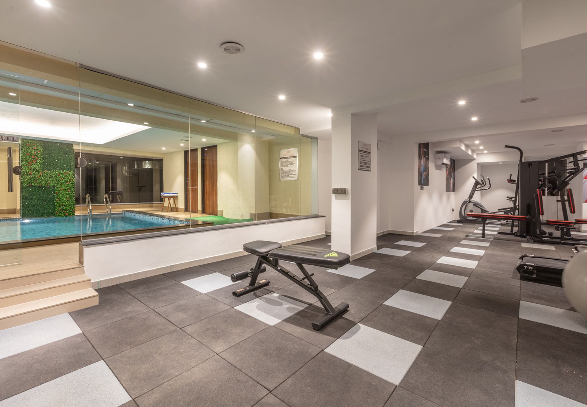 A modern gym with a pool, exercise equipment, and a mirrored wall.